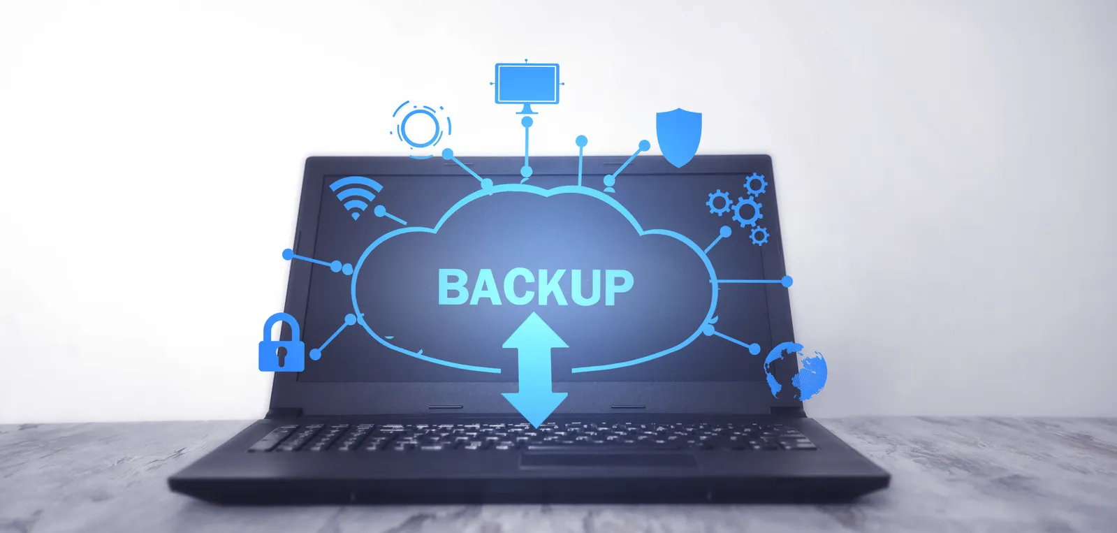 Laptop mit blauem Cloud‑Symbol und großem Schriftzug „BACKUP“ über der Tastatur